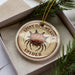 A round ornament with a spiny spider design, placed in a box with pine branches.