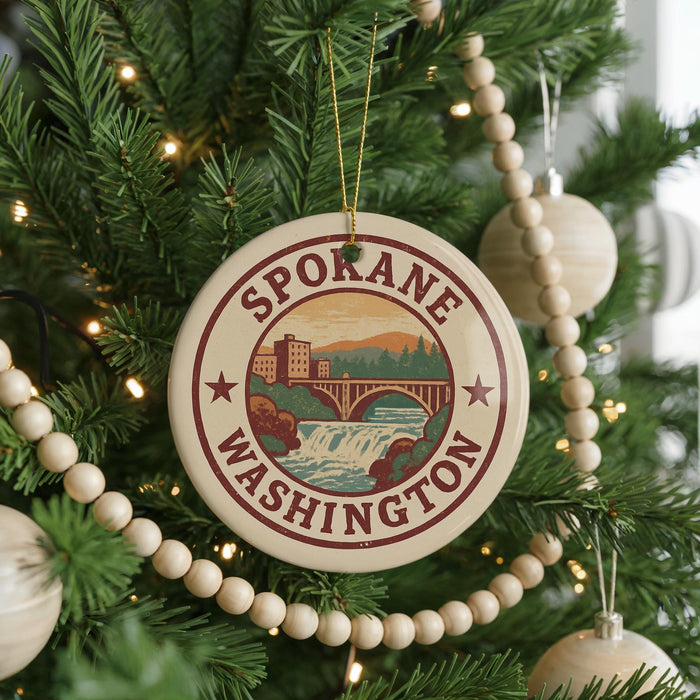 A round ornament on a Christmas tree, featuring the text "SPOKANE WASHINGTON" and an illustration of a bridge and waterfall.