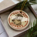 A round ornament with a monkey image and the text "SQUIRREL MONKEY" is displayed in a box, surrounded by pine branches.