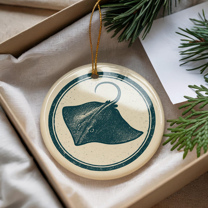 A decorative ornament featuring a stingray image is displayed in a box, surrounded by pine branches and a white card.