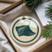 A decorative ornament featuring a stingray image is displayed in a box, surrounded by pine branches and a white card.