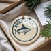 A round ornament with the text "SWORDFISH" and a graphic of a swordfish is displayed in a box, surrounded by pine branches.