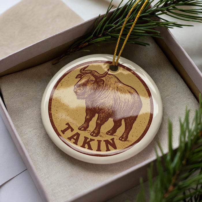 A ceramic ornament in a box, featuring a brown and tan design with a depiction of a yak and the word "Takin" written on it.
