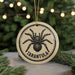 A round ornament with a black and white illustration of a tarantula on it, surrounded by a string of lights.