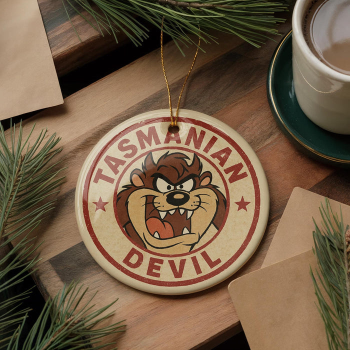 A round ornament featuring the Tasmanian Devil character from the animated series "The Tasmanians" is displayed on a wooden surface, surrounded by pine branches and a cup of coffee.