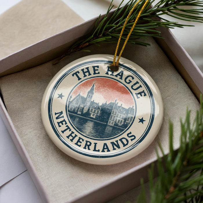 A decorative ornament in a box, featuring a circular design with a cityscape and the text "THE RAQUE NETHERLANDS".