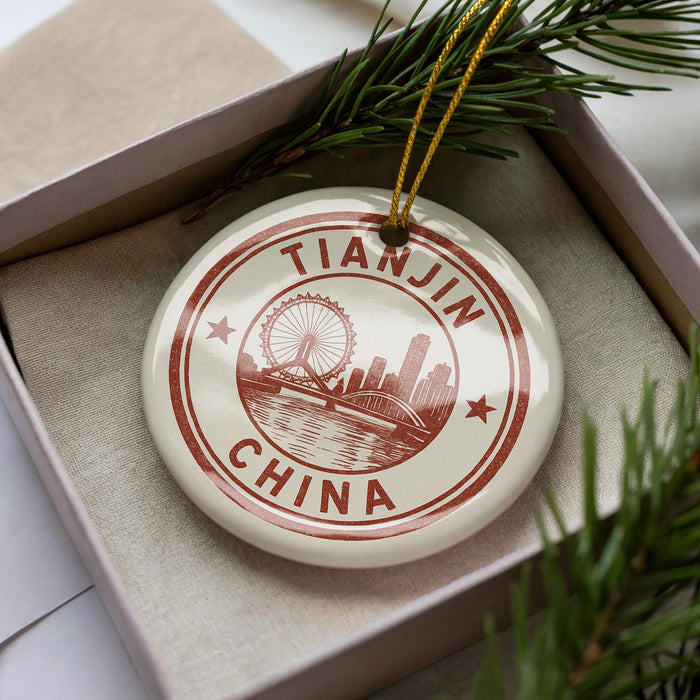 A decorative ornament in a box, featuring a circular design with a city skyline and a ferris wheel, along with the text "Tianjin China".
