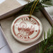 A decorative ornament in a box, featuring a circular design with a city skyline and a ferris wheel, along with the text "Tianjin China".