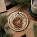 A Tibetan Mastiff ornament is displayed on a wooden surface, surrounded by pine branches and a cup of coffee.