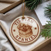 A Tibetan Spaniel ornament is displayed in a box, surrounded by pine branches.