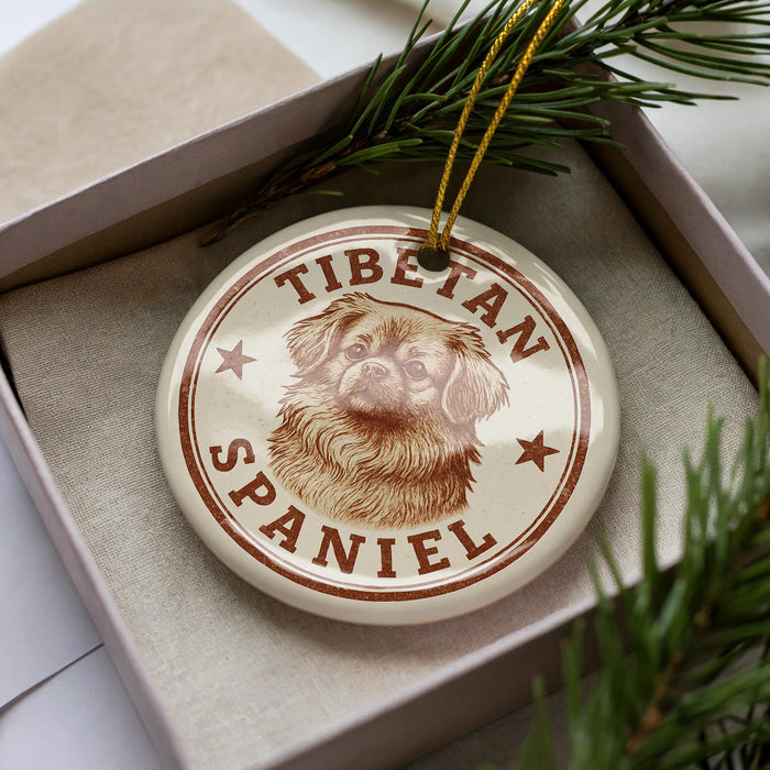 A Tibetan Spaniel ornament is displayed in a box, surrounded by pine branches.