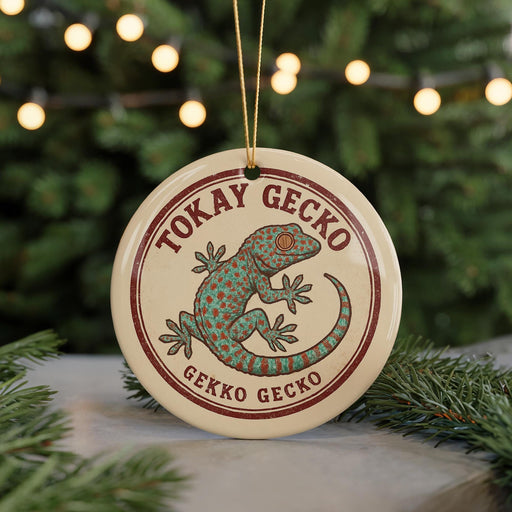 A round ornament featuring a green gecko with red spots, surrounded by greenery and a string of lights in the background.