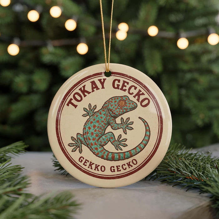A round ornament featuring a green gecko with red spots, surrounded by greenery and a string of lights in the background.