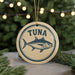 A round ornament with a blue and white design featuring a fish, specifically a tuna, is hanging from a string.