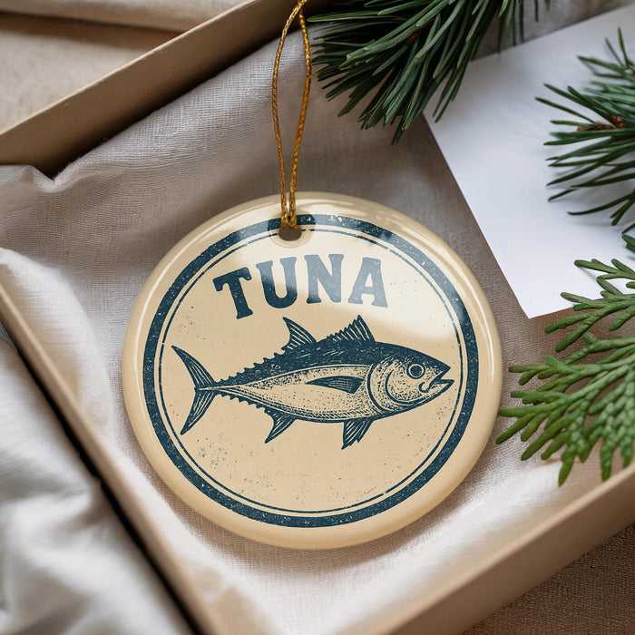 A round ornament with a fish design and the word "Tuna" printed on it, hanging from a string.