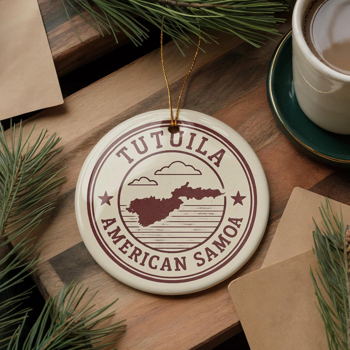 A circular ornament with the text "TUTUILA AMERICAN SAMOA" printed on it, surrounded by pine branches and a cup of coffee on a wooden surface.