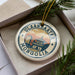 A circular ornament with the text "ULAANDAATAR MONGOLLI" printed on it, surrounded by a decorative border and a small illustration of a building.