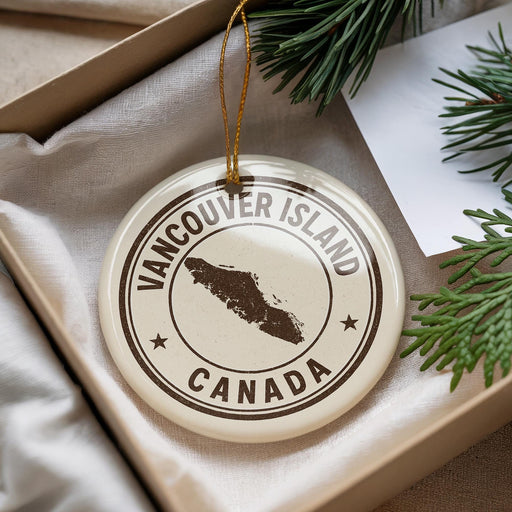 A white ornament with the text "VANCOUVER ISLAND CANADA" printed on it, along with a map of the region, is displayed in a box with pine branches.
