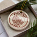 A decorative ornament with the text "VARANASI INDIA" on it, placed in a box with pine branches.