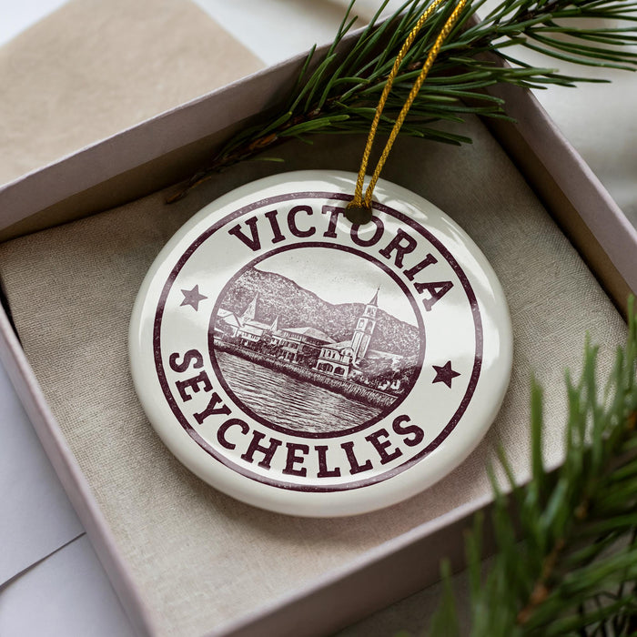 A decorative ornament with the name 'VICTORIA' and a picture of a town or city, placed in a box with pine branches.