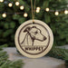 A round ornament featuring a drawing of a greyhound dog with the word "Whippet" written below it, hanging from a string.