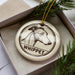 A ceramic ornament in the shape of a dog's head, with the word "WHIPPET" written below it, is displayed in a box with pine branches.