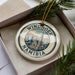 A decorative ornament with the text "WINDROek Namibia" on it, placed in a box with pine branches.