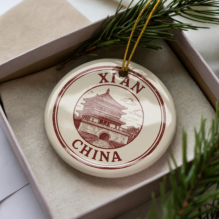 A decorative ornament in a box, featuring a circular design with a building and the text "XIAN CHINA" printed on it.