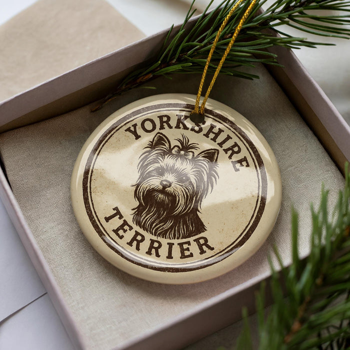 A decorative ornament featuring a Yorkshire Terrier dog's head, placed inside a box with pine branches.