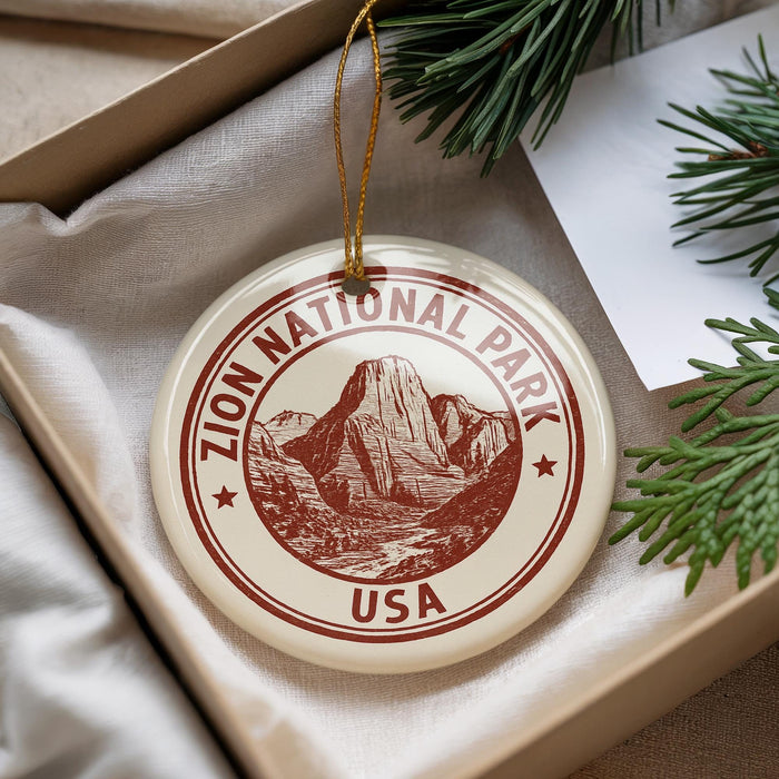 A round ornament with the inscription "ZION NATIONAL PARK USA" is displayed in a box, surrounded by pine branches.