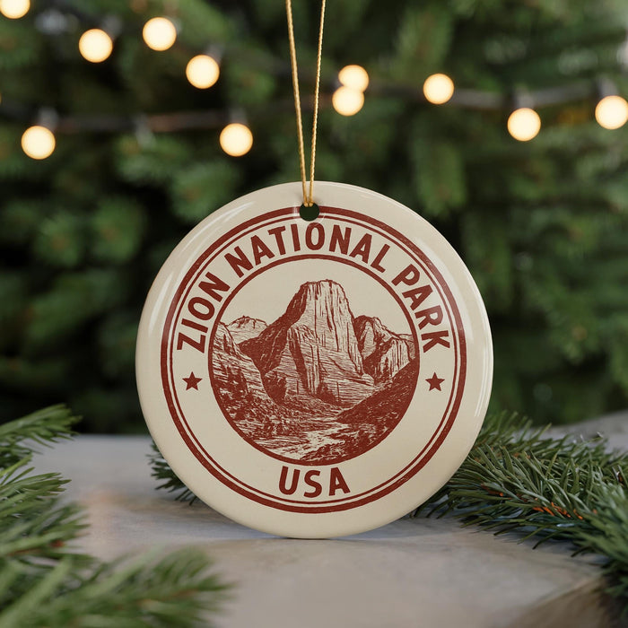 A circular ornament with the text "ZION NATIONAL PARK USA" and an illustration of a mountain range, hanging from a string.