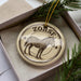 A circular ornament featuring a zebra illustration, placed in a box with pine branches.