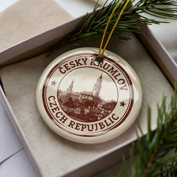 A decorative ornament in a box, featuring a circular design with a castle and the text "CESKY KRUMLOV Czech Republic".