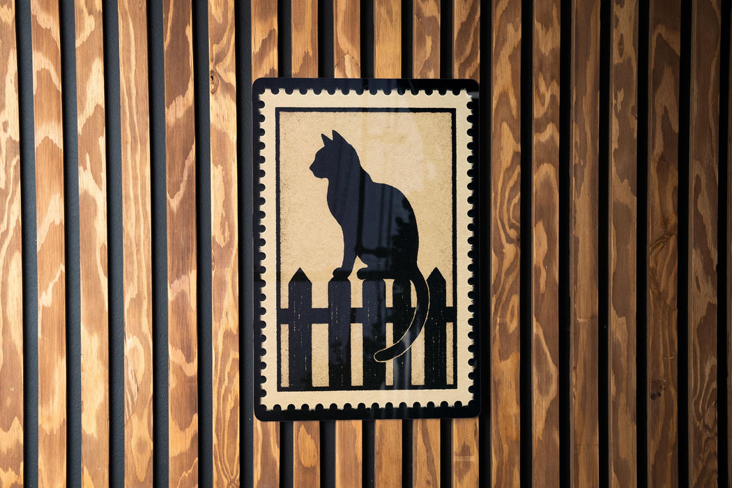 A black silhouette of a cat sitting on a wooden fence is displayed on a wooden wall.