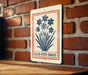 A sign with a blue flower design is hanging on a brick wall.