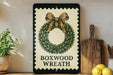 A decorative wreath with a bow on top, placed on a shelf next to a wooden cutting board and some lemons.