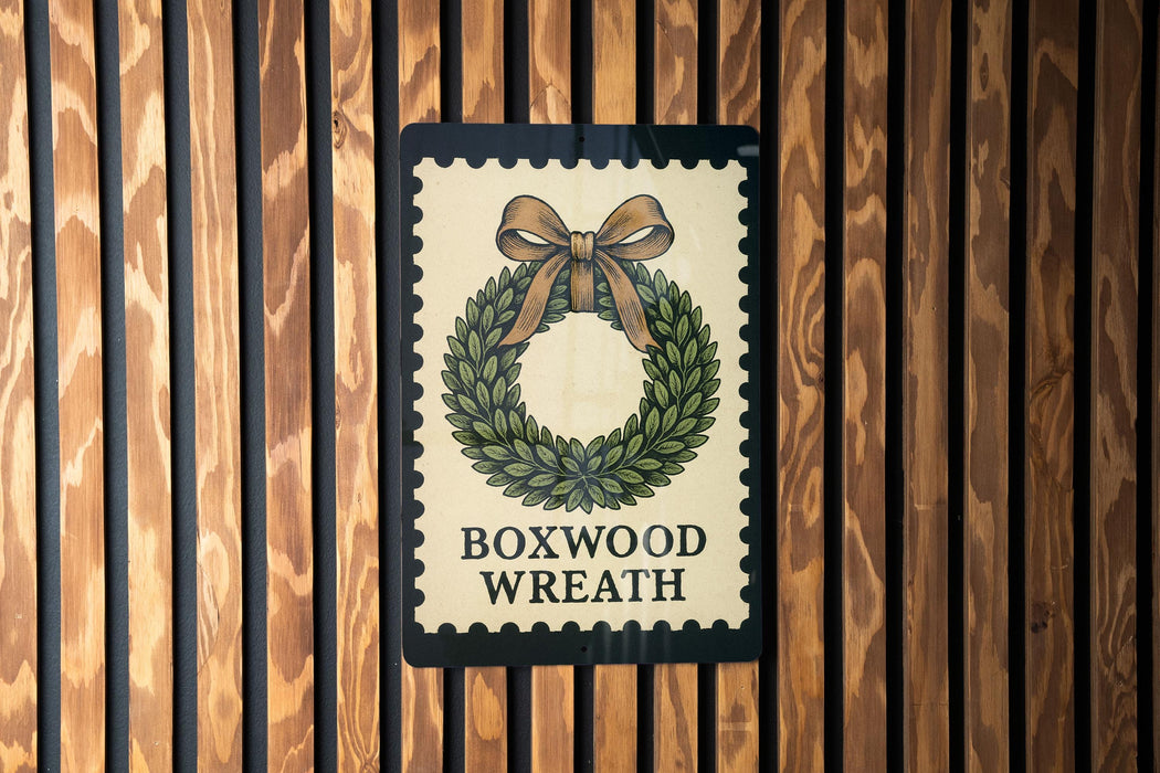 A sign with a wreath design and the text "BOXWOOD WRATH" is displayed on a wooden wall.