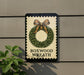 A sign for a "Boxwood Wreath" is displayed on a wall, with a wreath design and a brown ribbon bow.