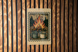 A metal sign with a wood-paneled background hangs on a wall, featuring an illustration of two mugs with a campfire in the background.