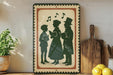A framed illustration of three people, likely depicting a family or group of friends, is displayed on a shelf next to a wooden cutting board and a potted plant.