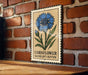 A decorative metal sign featuring a blue cornflower on a brick wall.