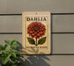 A decorative flower sign with the word "Dahlia" on it, mounted on a wall next to a plant.