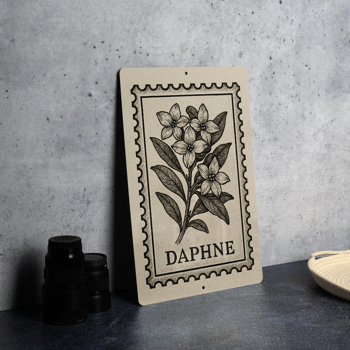 a framed print of a floral illustration with the word "DAPHNE" printed on it, placed on a table next to some black camera lenses.