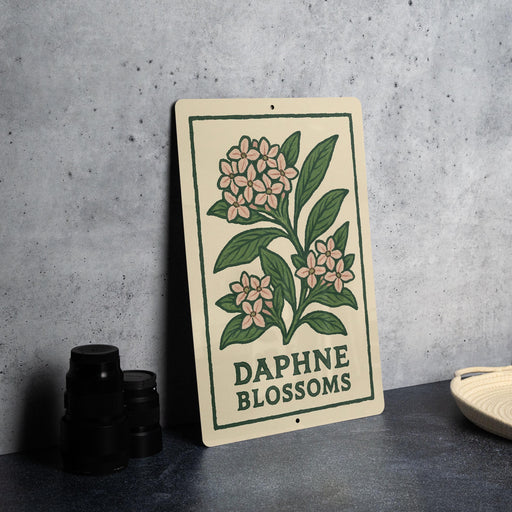 a sign with a floral design and the text "Daphne Blossoms" on it, placed on a table next to some black camera lenses.
