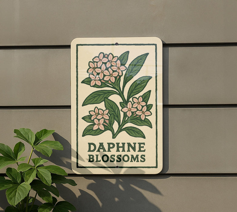 a sign with a floral design and the text "DAPHNE BLOSSOMS" on it, mounted on a wall next to a plant.