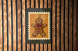 A gingerbread man illustration is displayed on a wooden wall, framed by a black border.