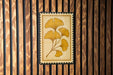 a framed artwork of yellow ginkgo leaves against a wooden background.