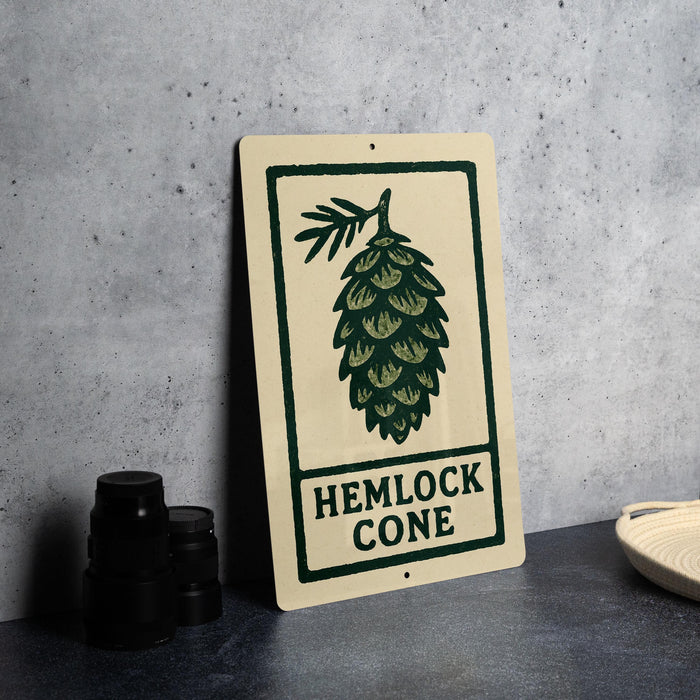 a sign with a pine cone design, placed on a countertop next to some black camera lenses.
