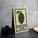 a sign with a pine cone design, placed on a countertop next to some black camera lenses.
