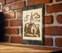 A framed illustration of a church with a steeple is displayed on a brick wall.